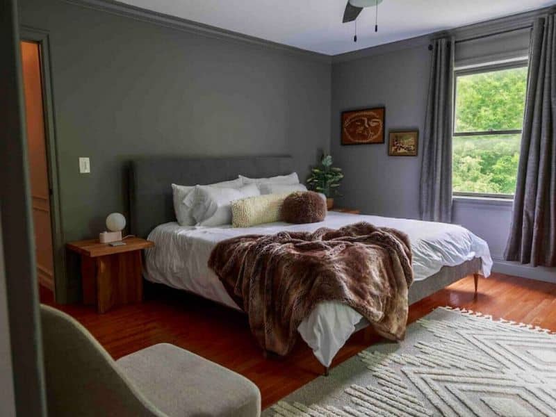 A neatly presented bedroom in a Catskills Vrbo rental, with a plush bed, grey walls, and a view of the greenery outside through a window.
