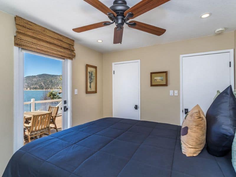 Bedroom with direct deck access in a Big Bear lakefront cabin rental, showcasing a large bed, ceiling fan, and a picturesque lake view.