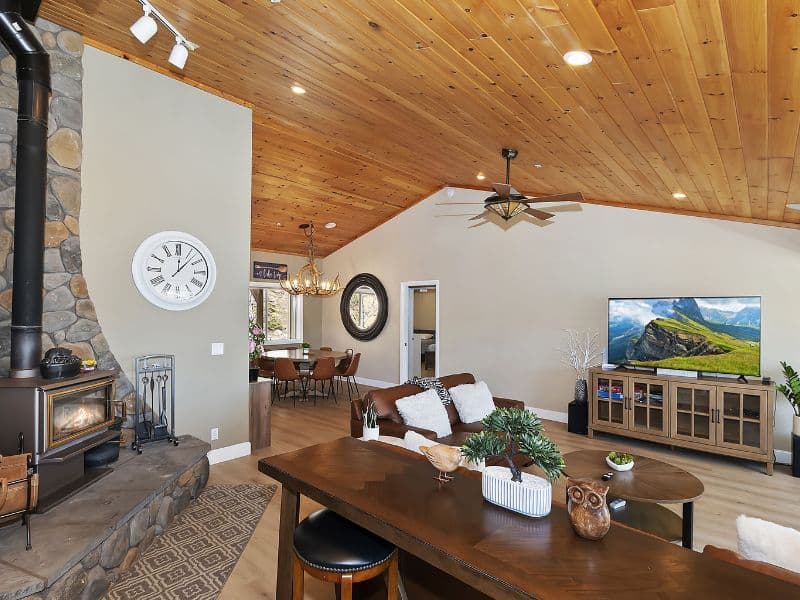 "Interior of a Big Bear rental with a high, wood-paneled ceiling, featuring a stone fireplace, modern furnishings, and a large flat-screen TV.
