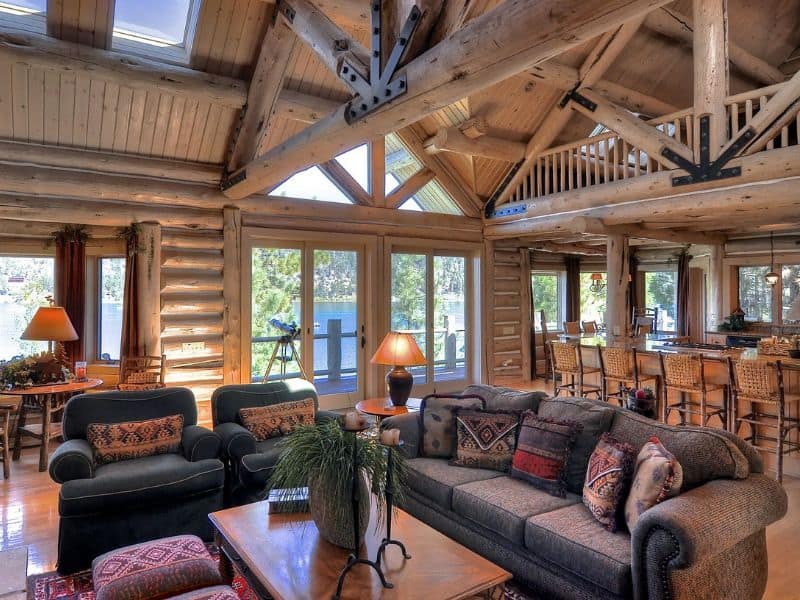 Spacious living room with high ceilings, exposed wooden beams, and large windows in a cabin with views over Big Bear Lake, CA.