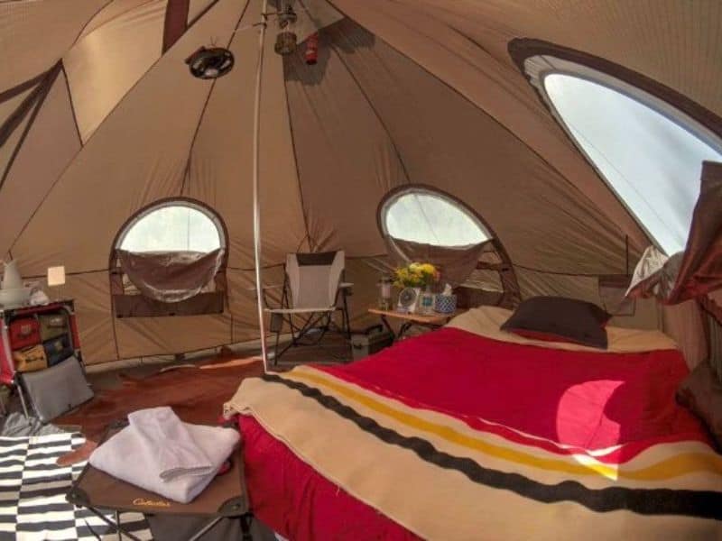 Interior view of an Arizona Luxury Expeditions tent featuring plush bedding and a circular chair.