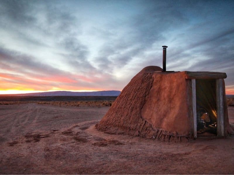 Traditional Navajo hogan at dusk with a warm glow against the expansive desert sky.