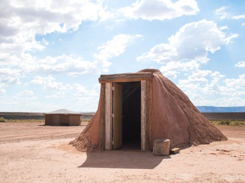 Daytime view of a traditional Navajo hogan's entrance with a clear blue sky overhead, providing a cultural stay for those glamping near the Grand Canyon.