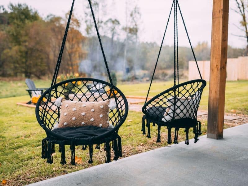 Outdoor seating area with two black boho-style hanging egg chairs by a fire pit at a Hocking Hills container home.