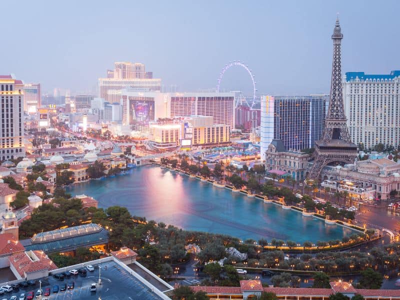 Aerial view of the Las Vegas Strip at dusk with illuminated buildings and the replica Eiffel Tower.