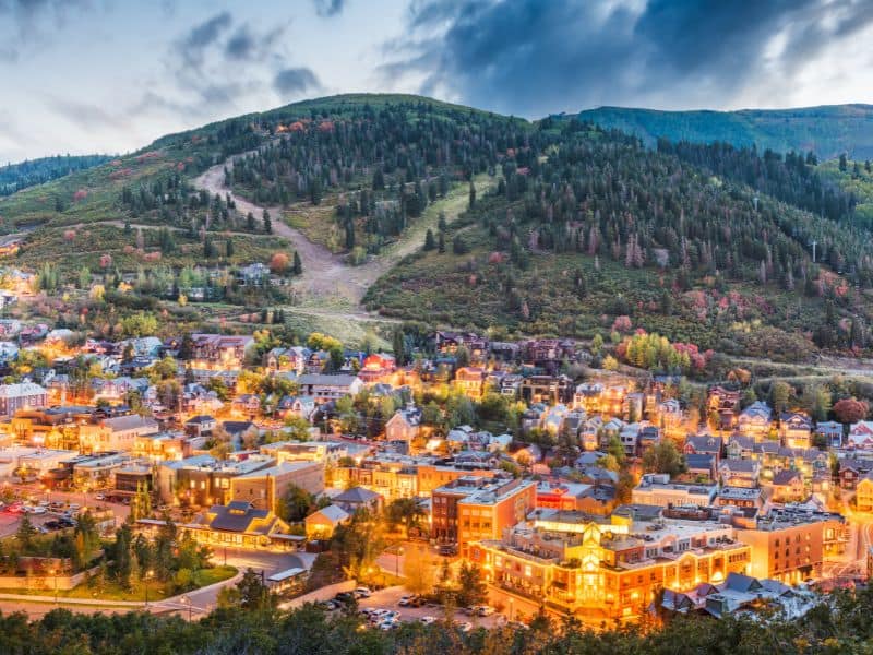 Twilight view of Park City, Utah, with illuminated buildings and a backdrop of forested hills, a stop on the route from Los Angeles to Yellowstone.