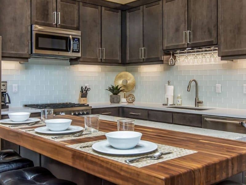 Modern kitchen setup with dark wood cabinetry, a large wooden island set for dining, and stainless steel appliances in a Moab vacation rental at Sage Creek.