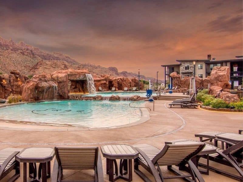 Resort-style community pool with natural rock features and ample lounging chairs at Sage Creek vacation rentals, set against a backdrop of rugged mountains.