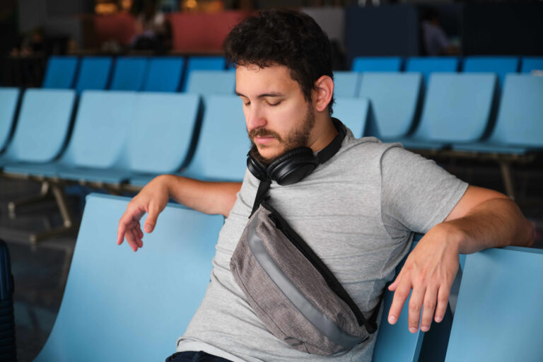 Man trying to sleep at Narita airport, sad because his flight was delayed.